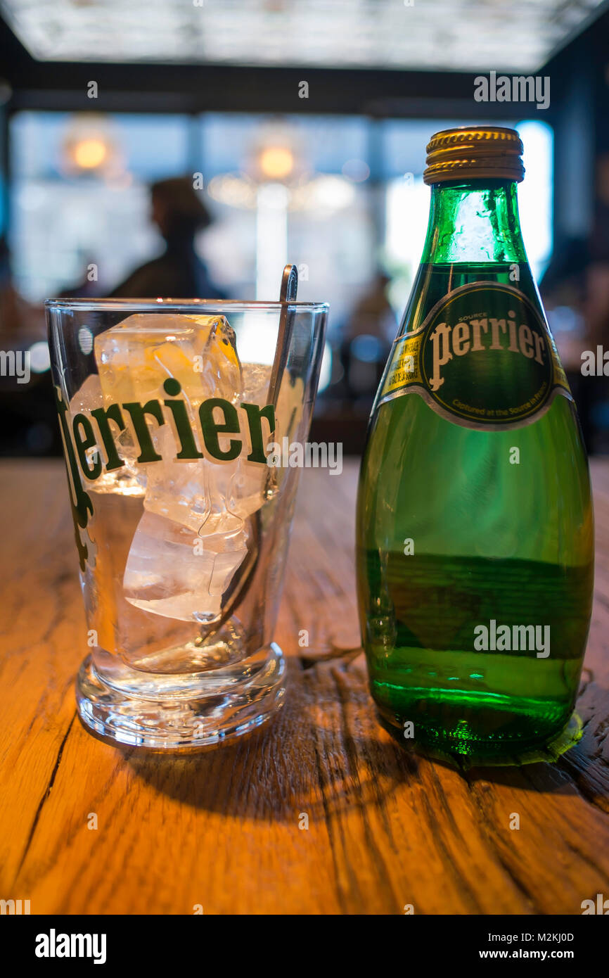 Un bicchiere e una bottiglia di spumante freddo Perrier acqua minerale in uno stile francese café Foto Stock