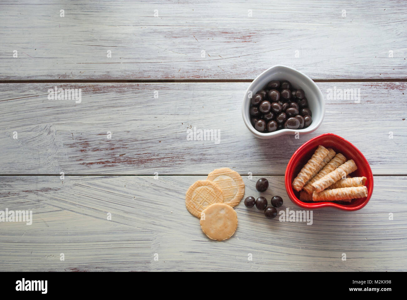 Due forma di cuore ciotole con biscotti e caramelle su vintage superficie di legno. concetto di celebrazione il giorno di San Valentino e un pezzo di amore, sano cibo organico Foto Stock