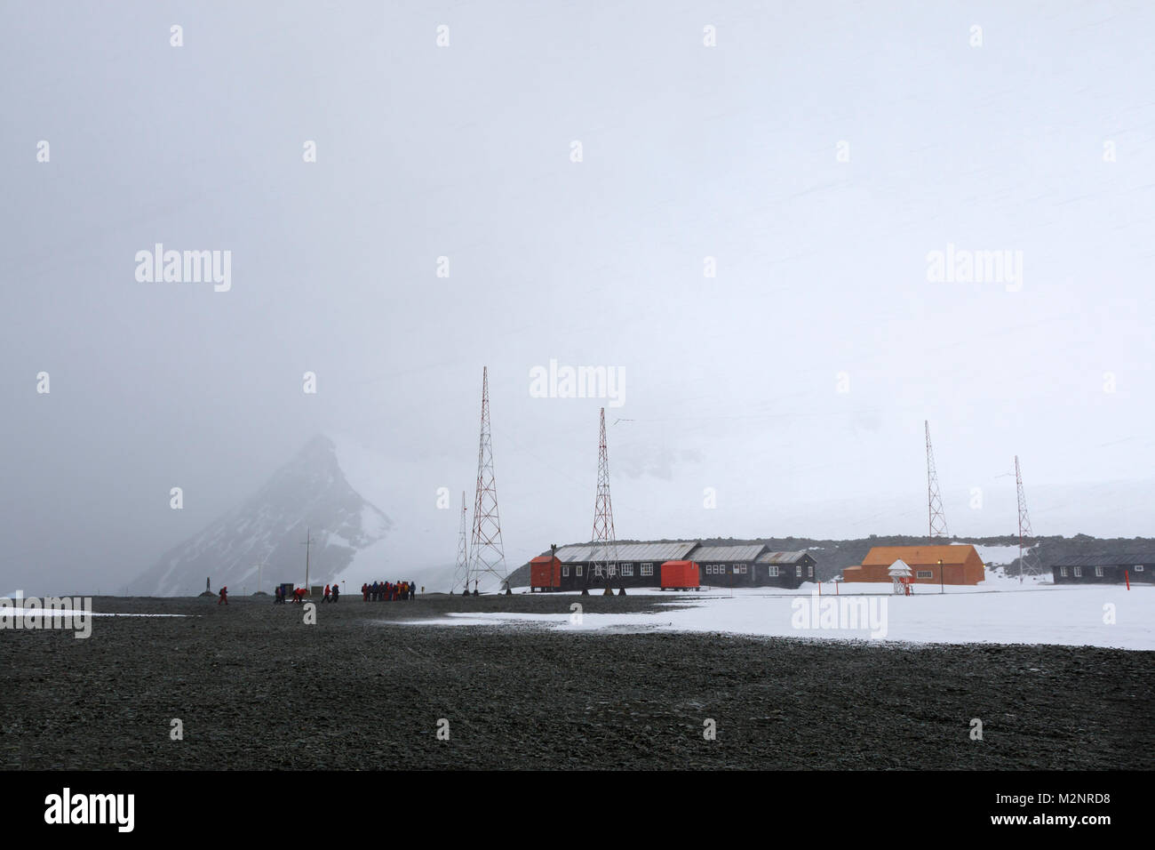 Panorama Eco turisti visitano remota stazione antartica durante la tempesta di neve di vento orizzontale di lavori di soffiaggio della neve bianco sullo sfondo di montagna alte antenne radio Foto Stock