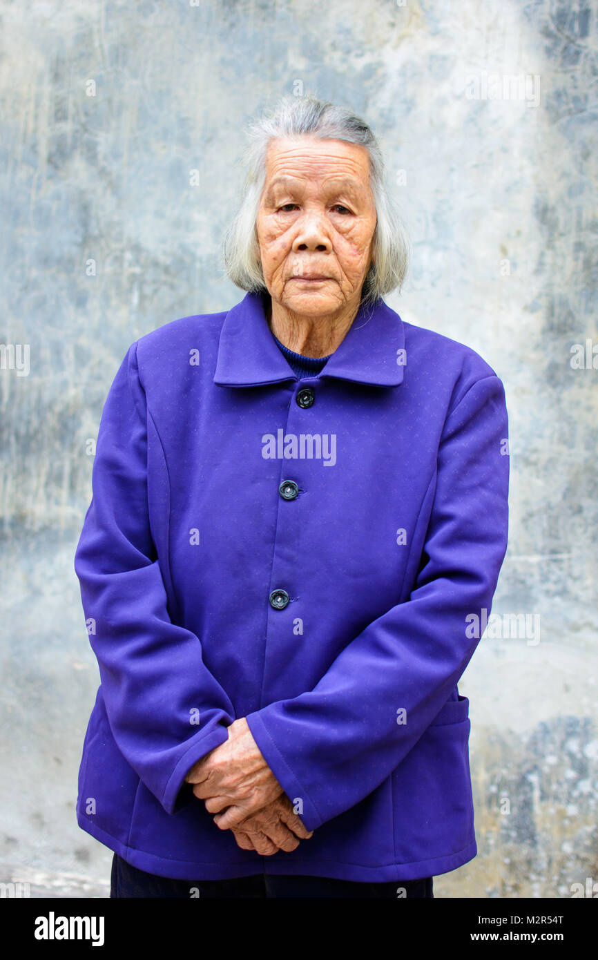 Ritratto di senior donna asiatica in piedi contro la parete vintage Foto Stock