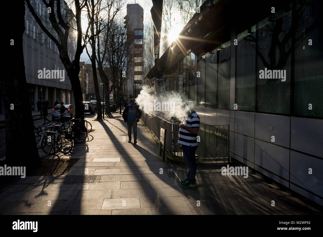 Un vaper espira una nuvola di fumo in condizioni di intensa luce solare in inverno, su un central London street, il 6 febbraio 2018, a Londra, in Inghilterra. Foto Stock