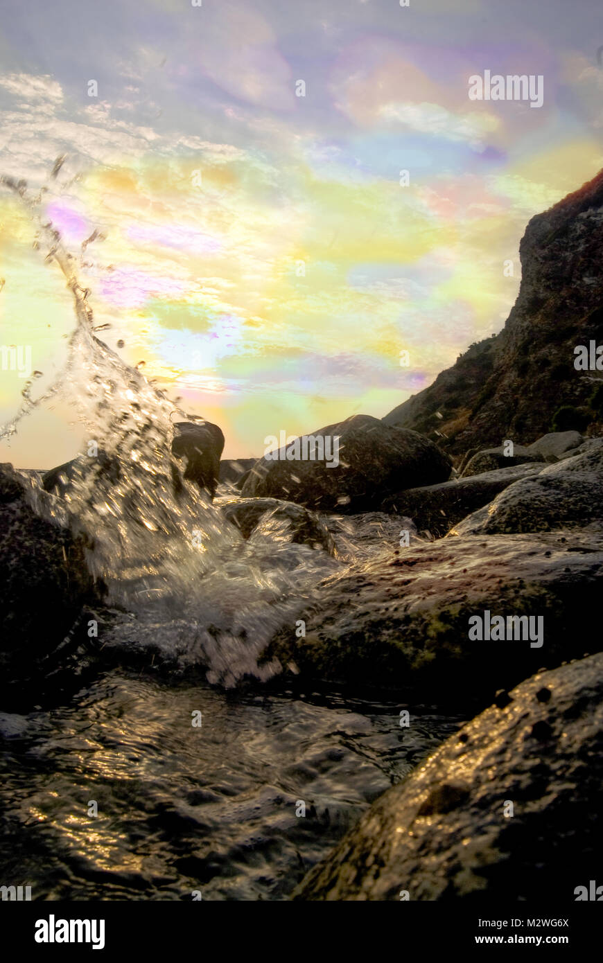 Mare schizza su una scogliera con un tramonto colorato Foto Stock