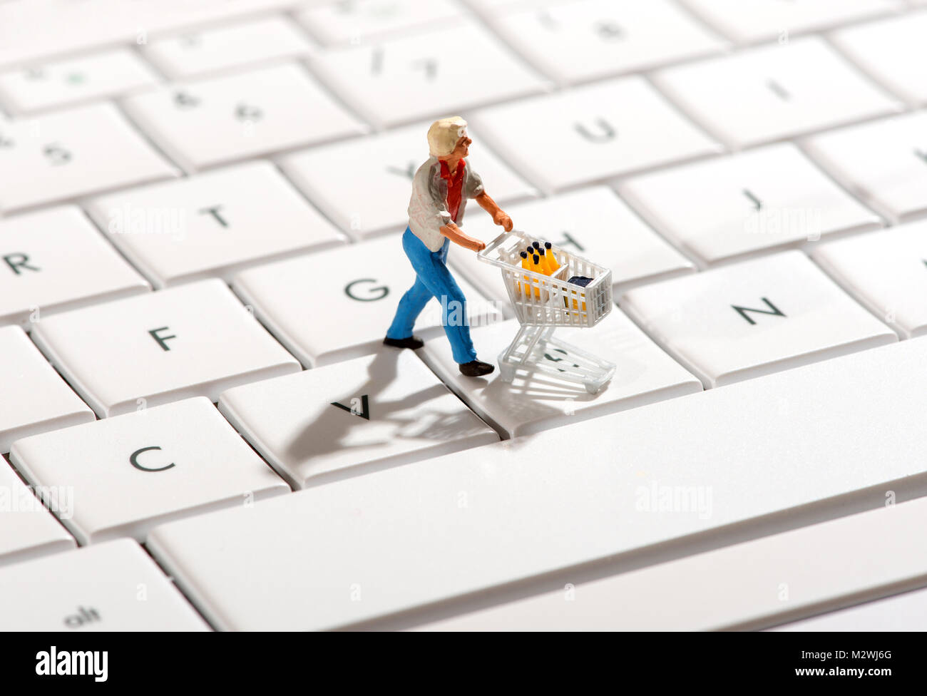 Statuetta in miniatura di una shopper spingendo un carrello sulla tastiera di un computer in un concetto di online o acquisti via internet Foto Stock