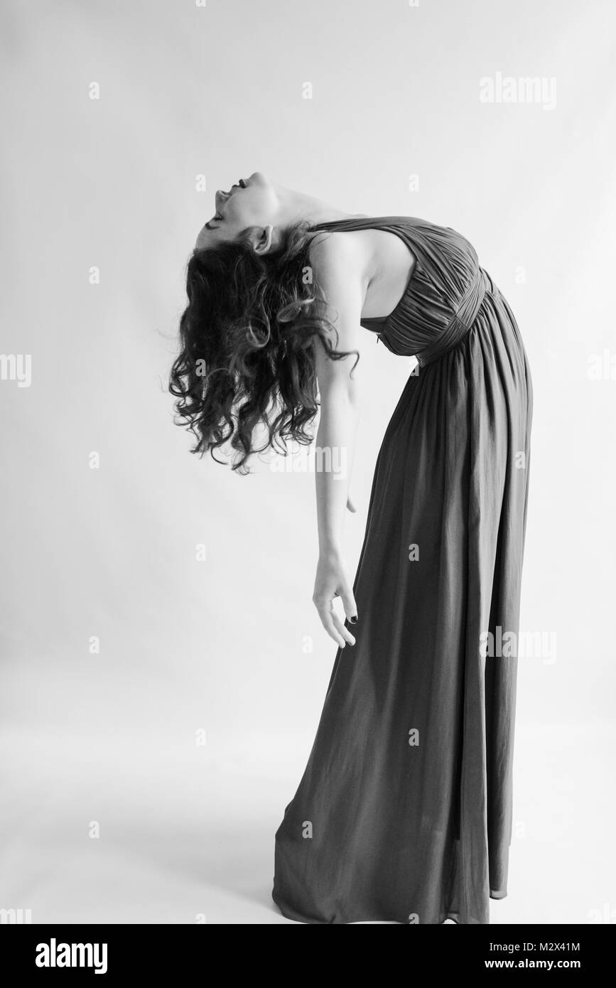 Bellissimo vestito in stile classico giovane ragazza danze attraverso un fondale grigio isolato. Abito lungo e capelli lunghi monotono Foto Stock
