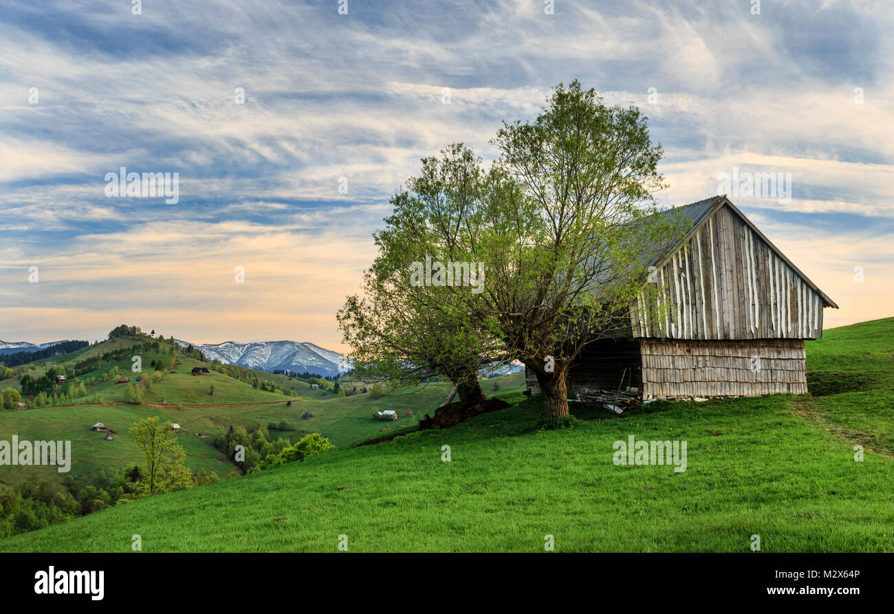 Fattoria rurale con la vecchia capanna in legno al tramonto vicino di crusca, Transilvania, Romania Foto Stock