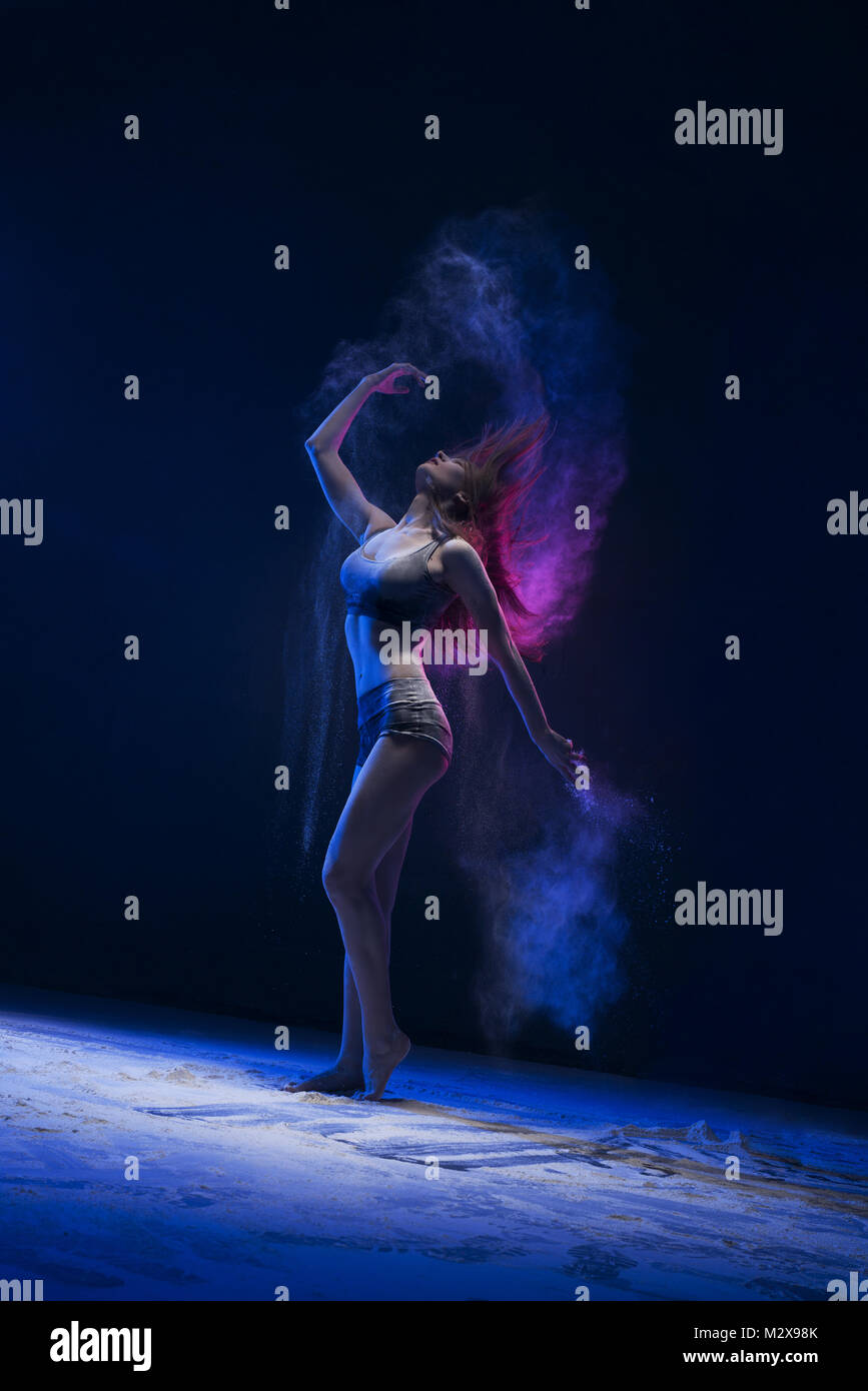 Slim girl dancing in blu di una nube di polvere di vista di profilo Foto Stock