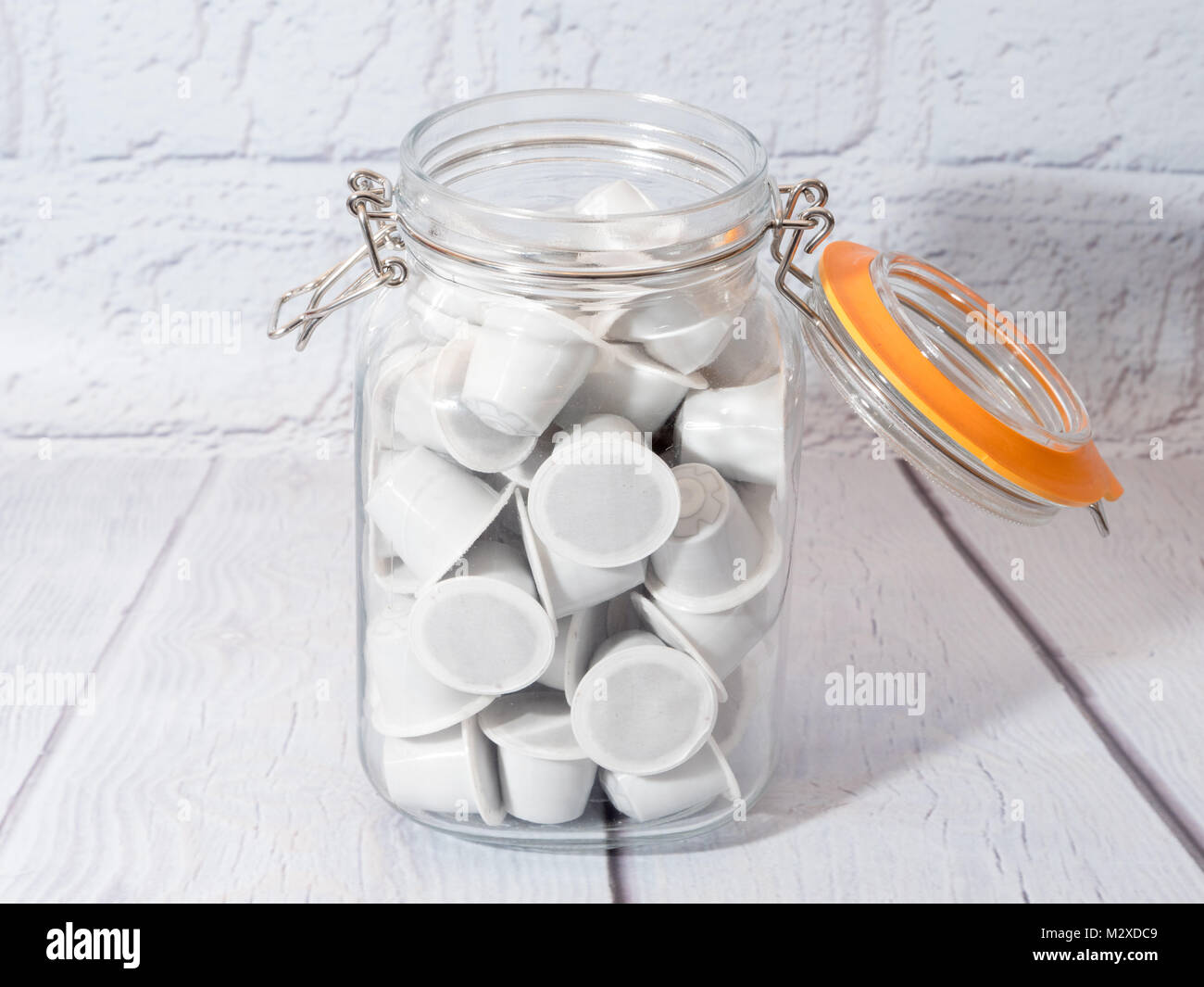 Un vaso di vetro pieno di bianco generico nespresso montare le cialde di caffè Foto Stock