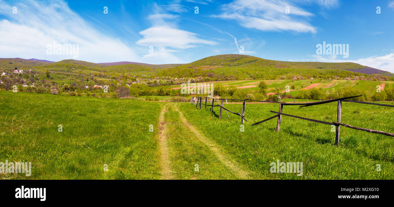 Panorama di montagna zona rurale in primavera. un paesaggio incantevole scenario con staccionata in legno lungo la strada del paese nella periferia del paese Foto Stock