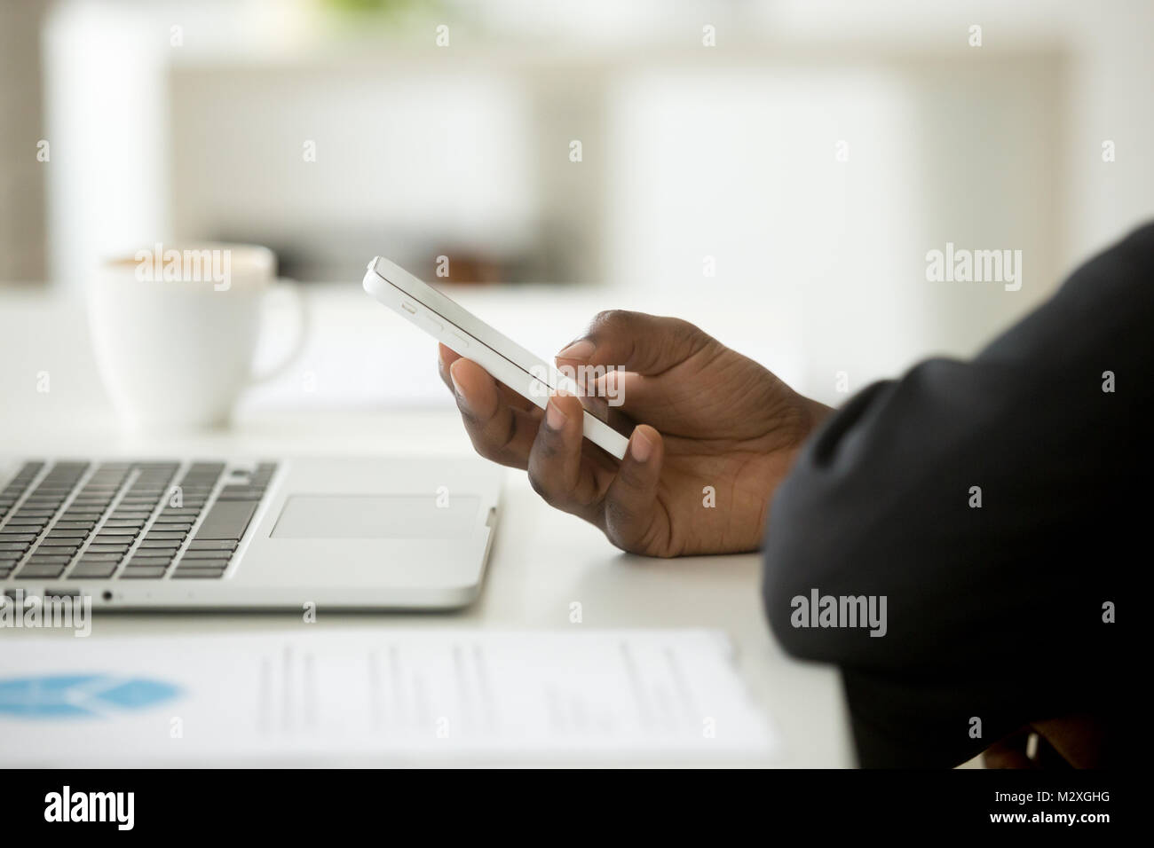 African-american imprenditore nel soddisfare tramite cellulare in ufficio, uomo nero smartphone tenuta presso il luogo di lavoro con computer laptop, dispositivi aziendali a Foto Stock