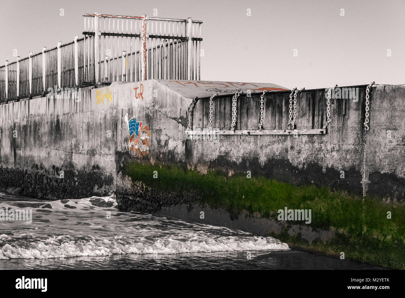 Bianco & Nero Foto di un pontile sulla spiaggia sulla costa della California con graffitis e muschio verde in colori a stato Dockweiler Beach in Playa del Rey, CA. Foto Stock