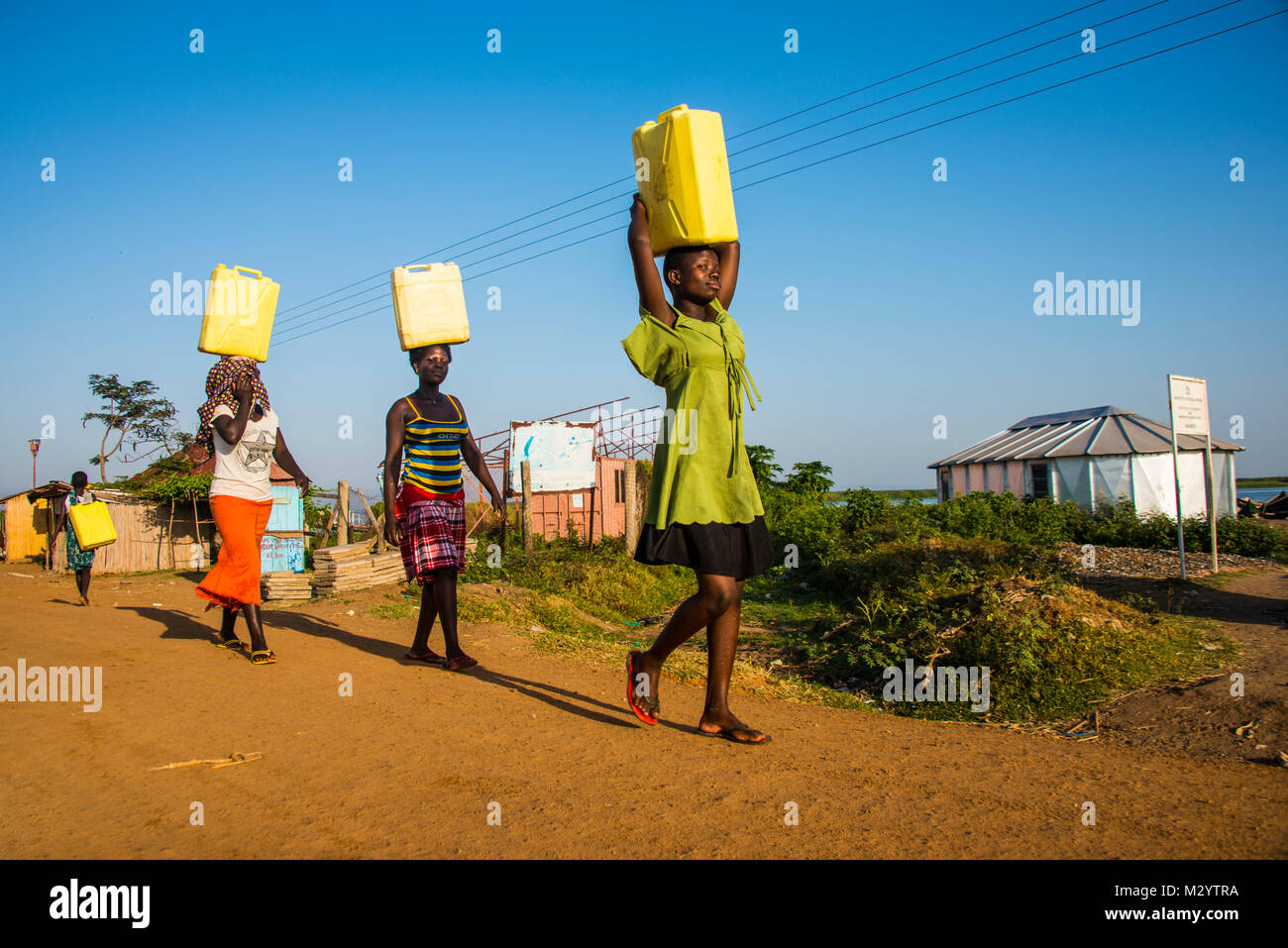 Le donne che trasportano contenitori di acqua sulla loro testa portando acqua home dal lago Albert, Uganda, Africa Foto Stock