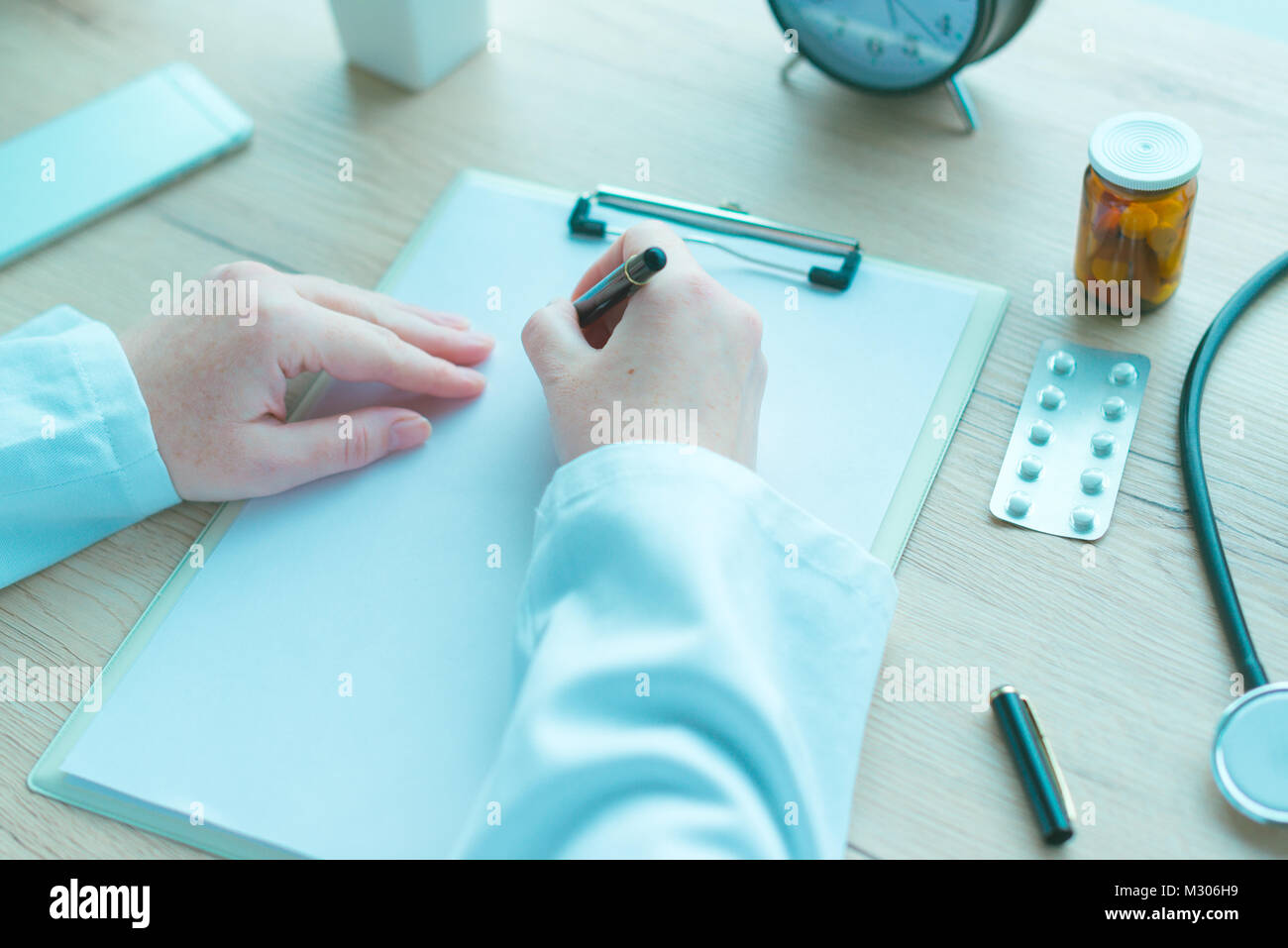 Medico di medicina generale scrivere appunti durante la visita medica, la prescrizione medicina e sanità, nei toni del blu immagine Foto Stock