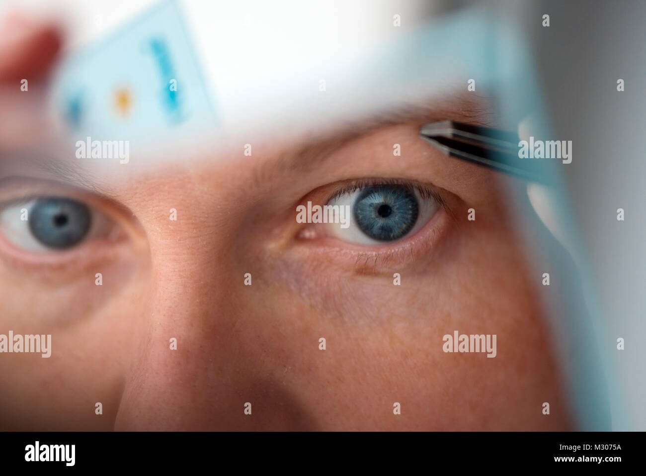 Donna spiumatura sopracciglia con pinzette dalla finestra, il fuoco selettivo Foto Stock