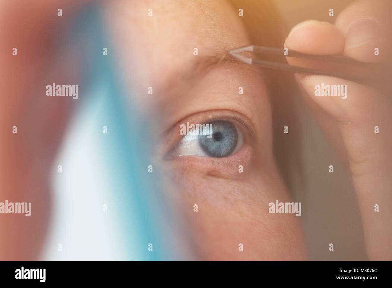 Donna spiumatura sopracciglia con pinzette dalla finestra, il fuoco selettivo Foto Stock