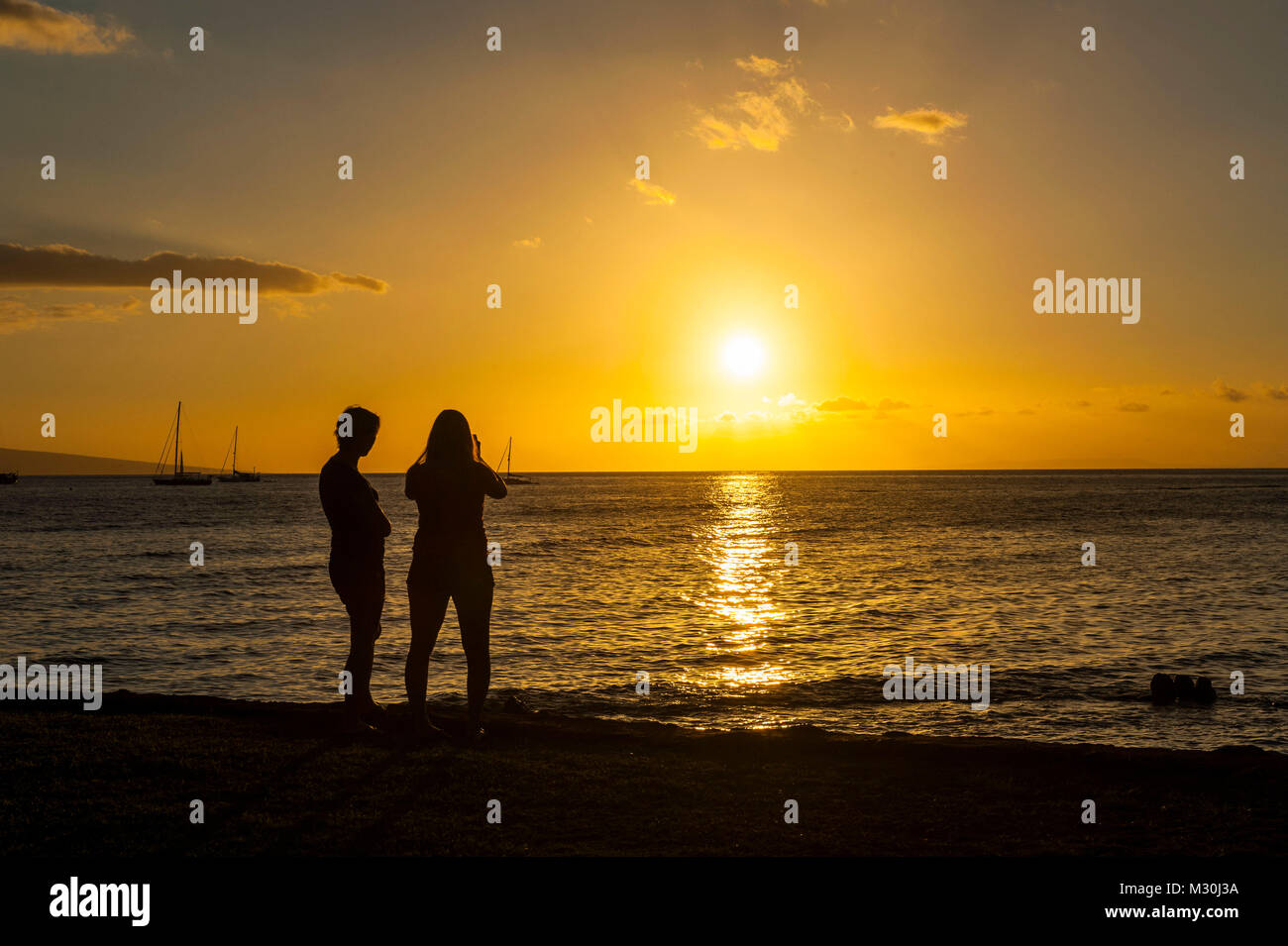 Tourist guardare il sole andare giù in un piccolo parco in Lahaina, Maui, Hawaii Foto Stock