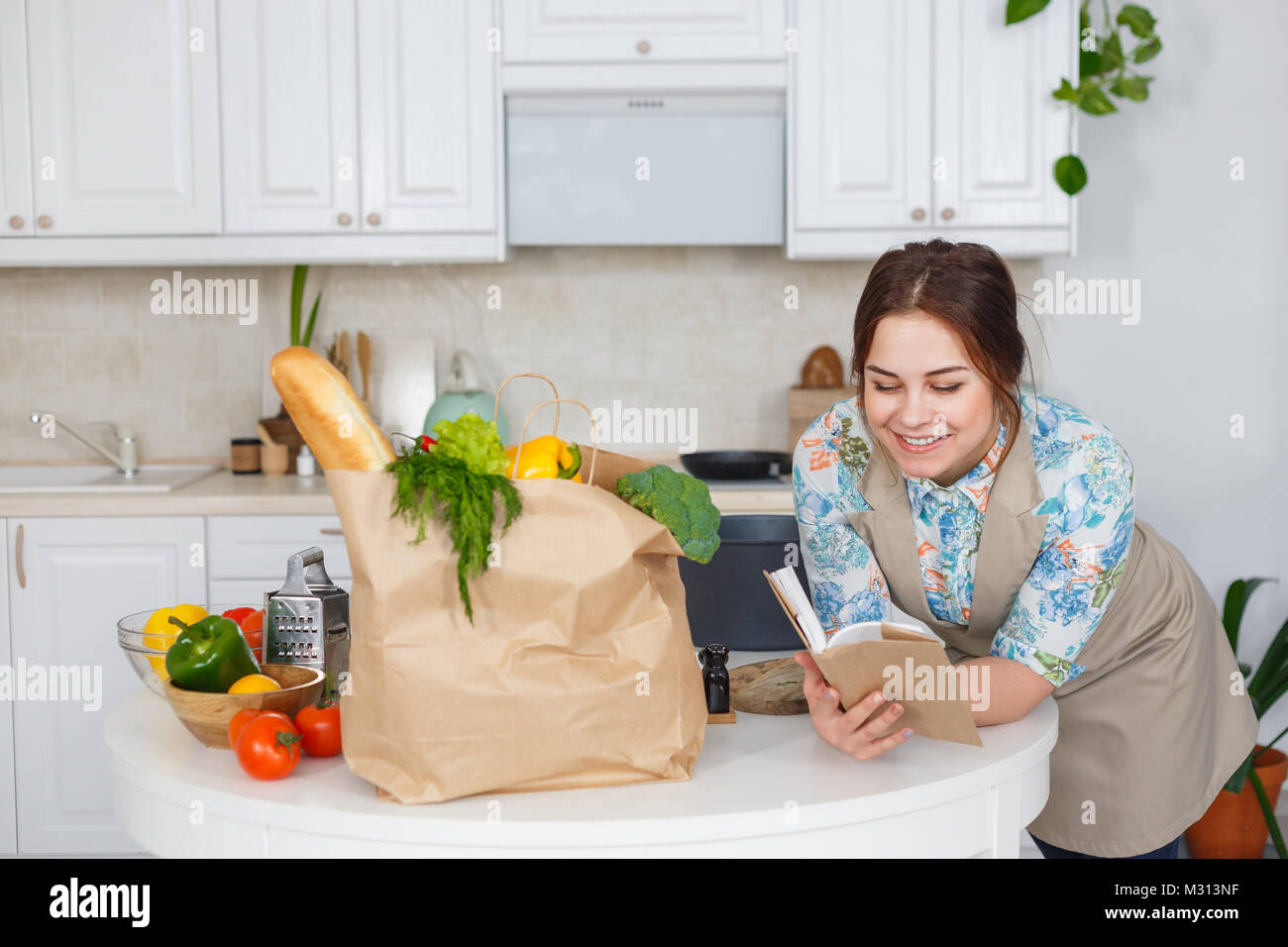 Sorridente giovane massaia la lettura di un libro di ricette vegetariane Foto Stock