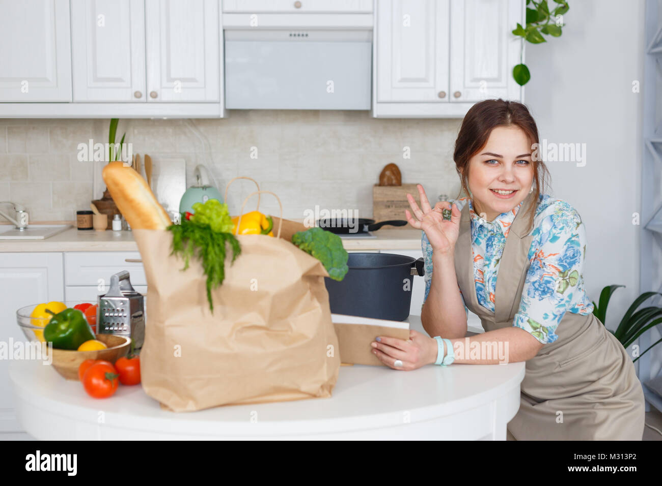 Giovani casalinga gesticolando ok con il libro di ricette di cucina. Foto Stock