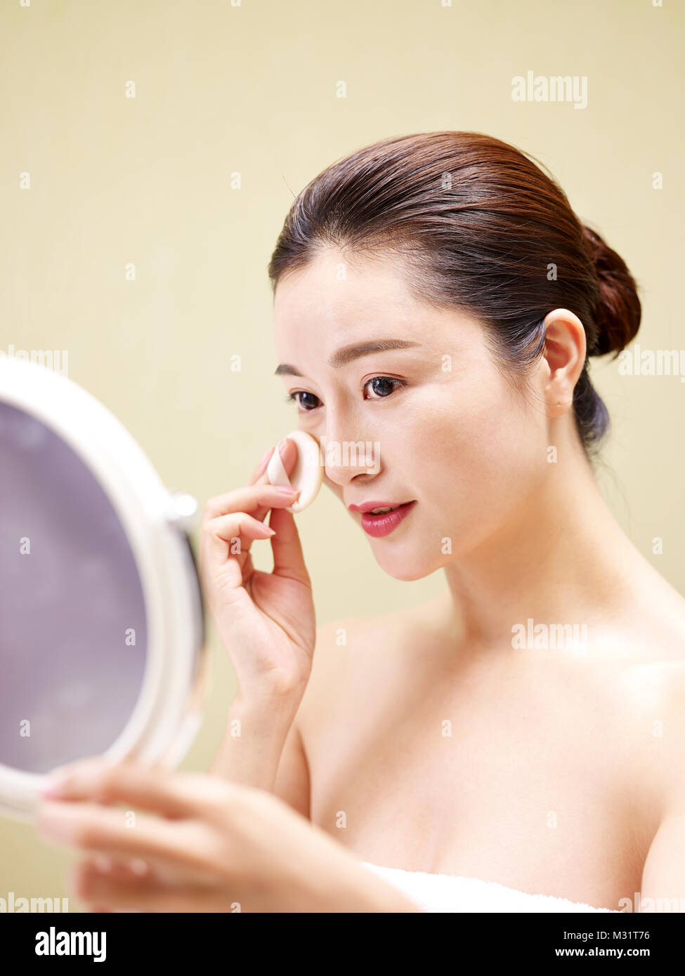 Bella giovane donna asiatica guardando nello specchio mentre la detersione viso con una spugna Foto Stock