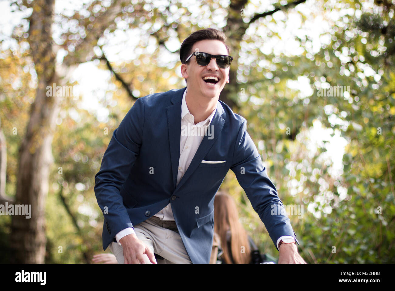 Giovane imprenditore in sella ad una bicicletta blu all'aperto in un parco. In viaggio per lavoro in bicicletta. Foto Stock