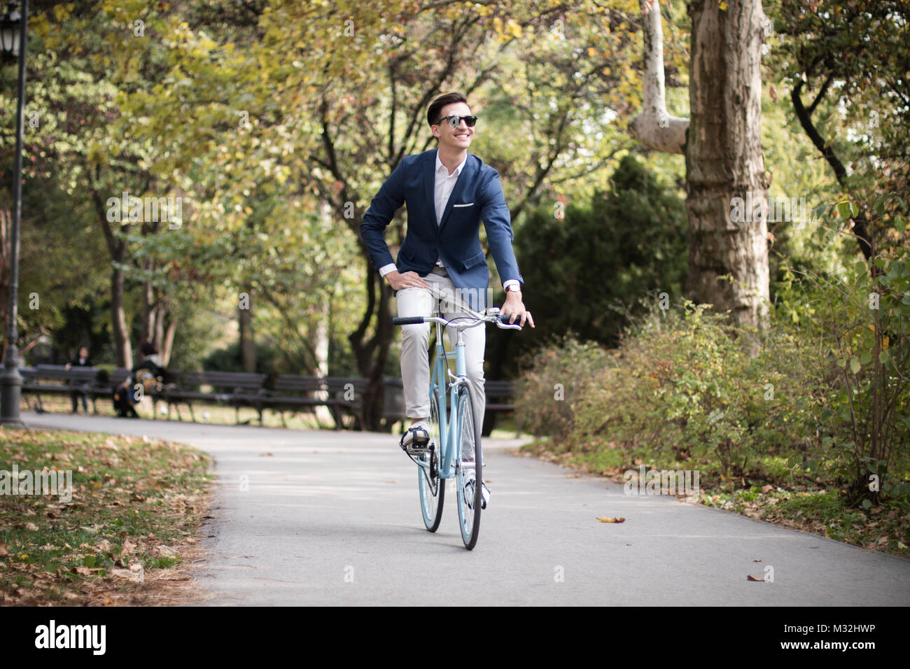 Giovane imprenditore in sella ad una bicicletta blu all'aperto in un parco. In viaggio per lavoro in bicicletta. Foto Stock