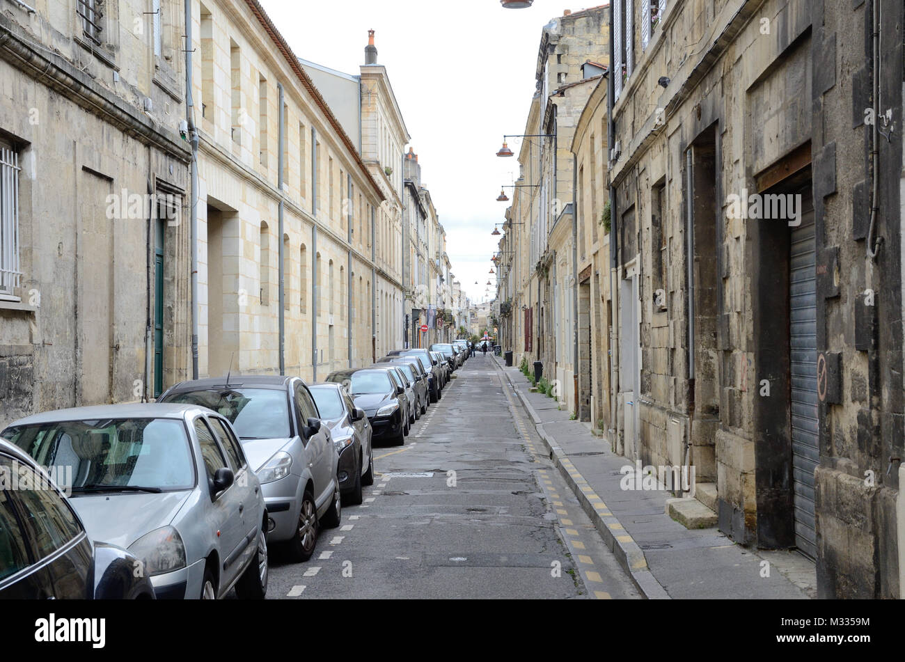 Molti moderni le macchine vengono parcheggiate a lato della antica stretta strada diritta nella città francese Bordeaux. Foto Stock