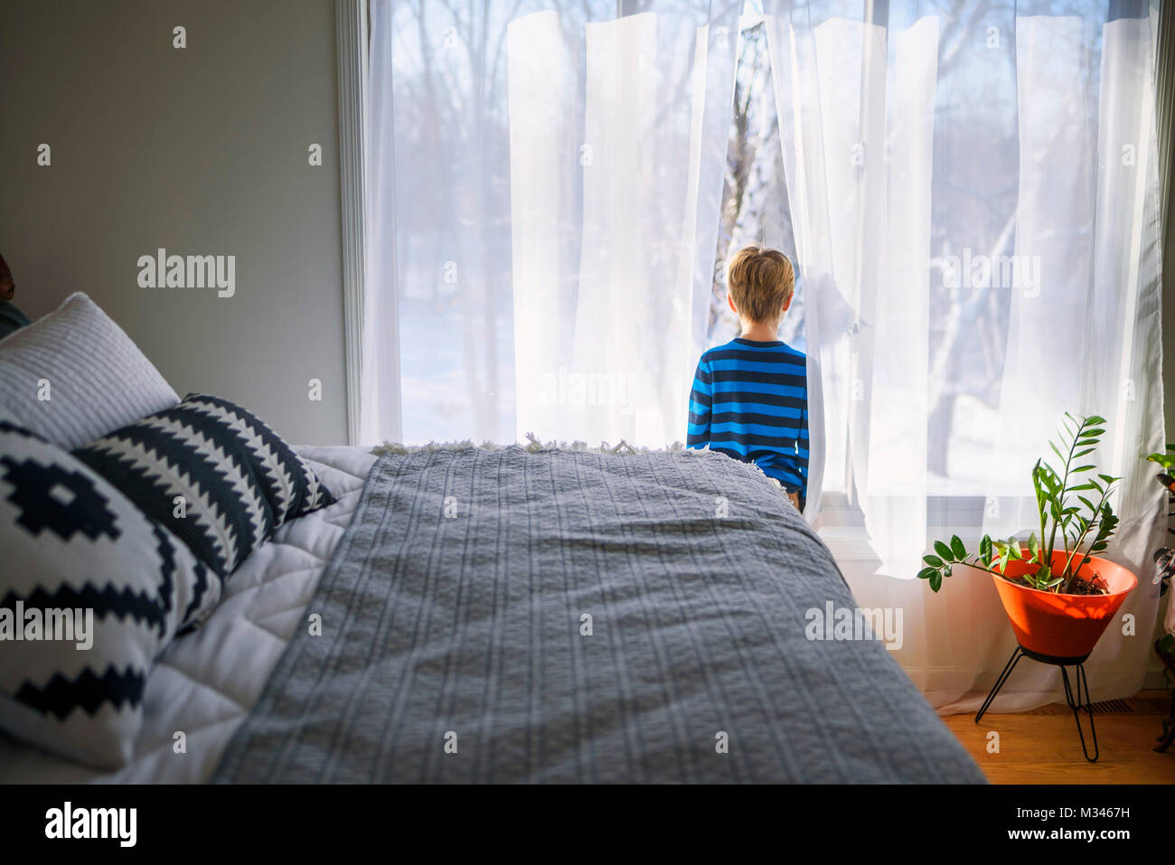 Ragazzo in piedi in camera da letto guardando fuori di una finestra in corrispondenza della neve Foto Stock