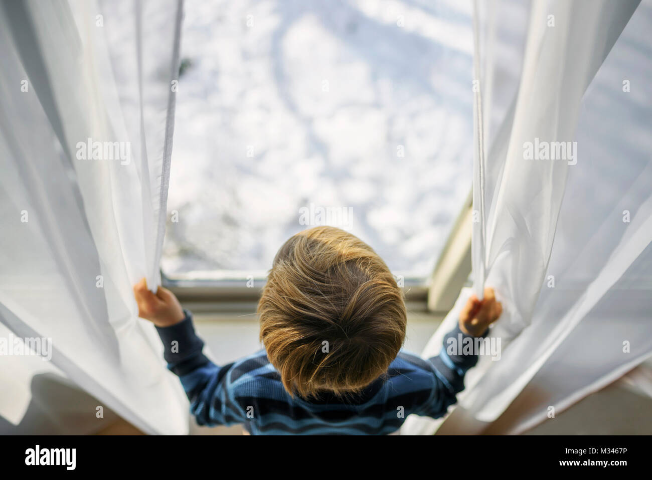 Ragazzo che guarda fuori da una finestra a neve Foto Stock