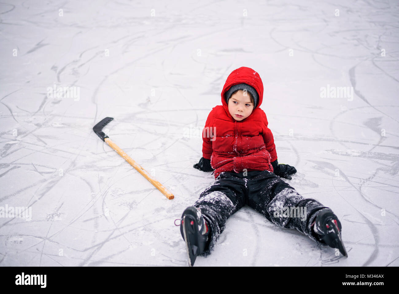 Ragazzo seduto sul ghiaccio con la sua mazza da hockey Foto Stock