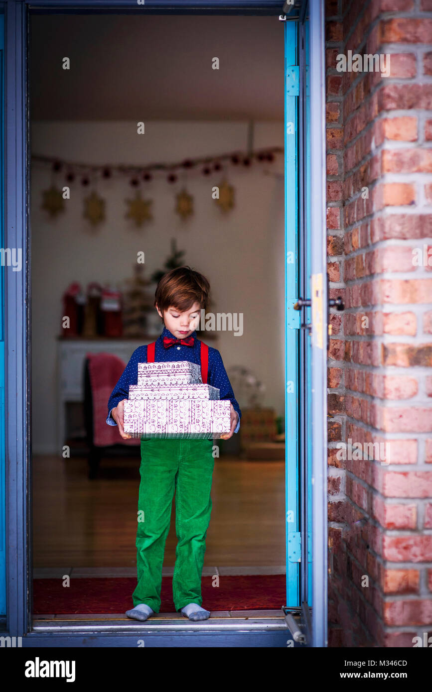 Ragazzo in piedi in una porta una catasta di avvolgere i regali di Natale Foto Stock
