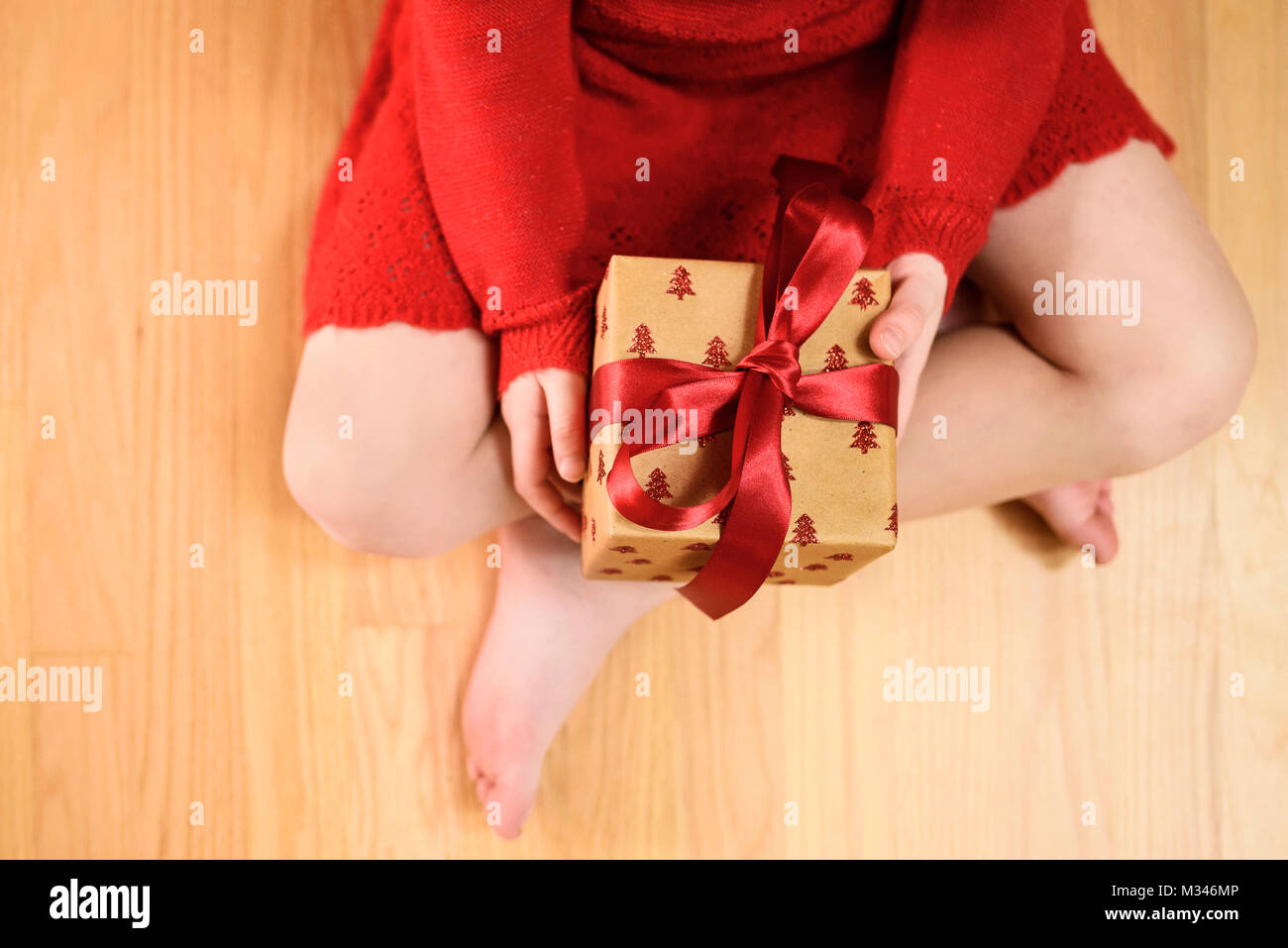 Vista dall'alto di una ragazza seduta a gambe incrociate sul pavimento con un regalo di Natale Foto Stock