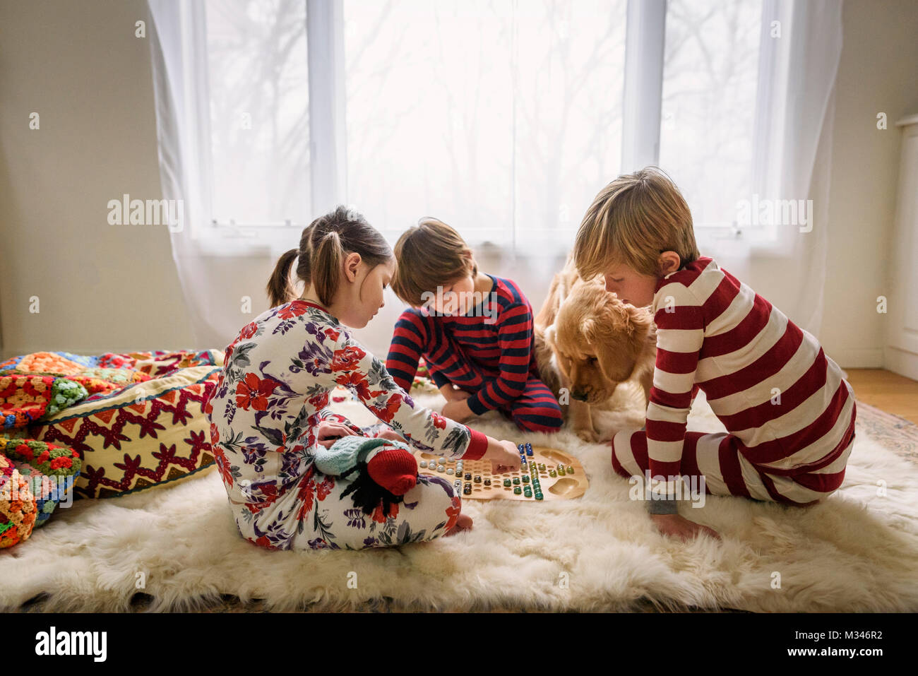 Tre bambini seduti sul pavimento con la loro golden retriever cane la riproduzione di un gioco da tavolo Foto Stock