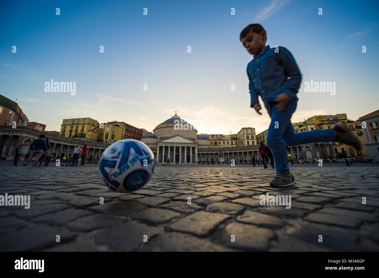 Napoli, Italia - circa ottobre 2017, giovane ragazzo giocando a calcio con motion blur sulla pavimentazione della piazza. Foto Stock