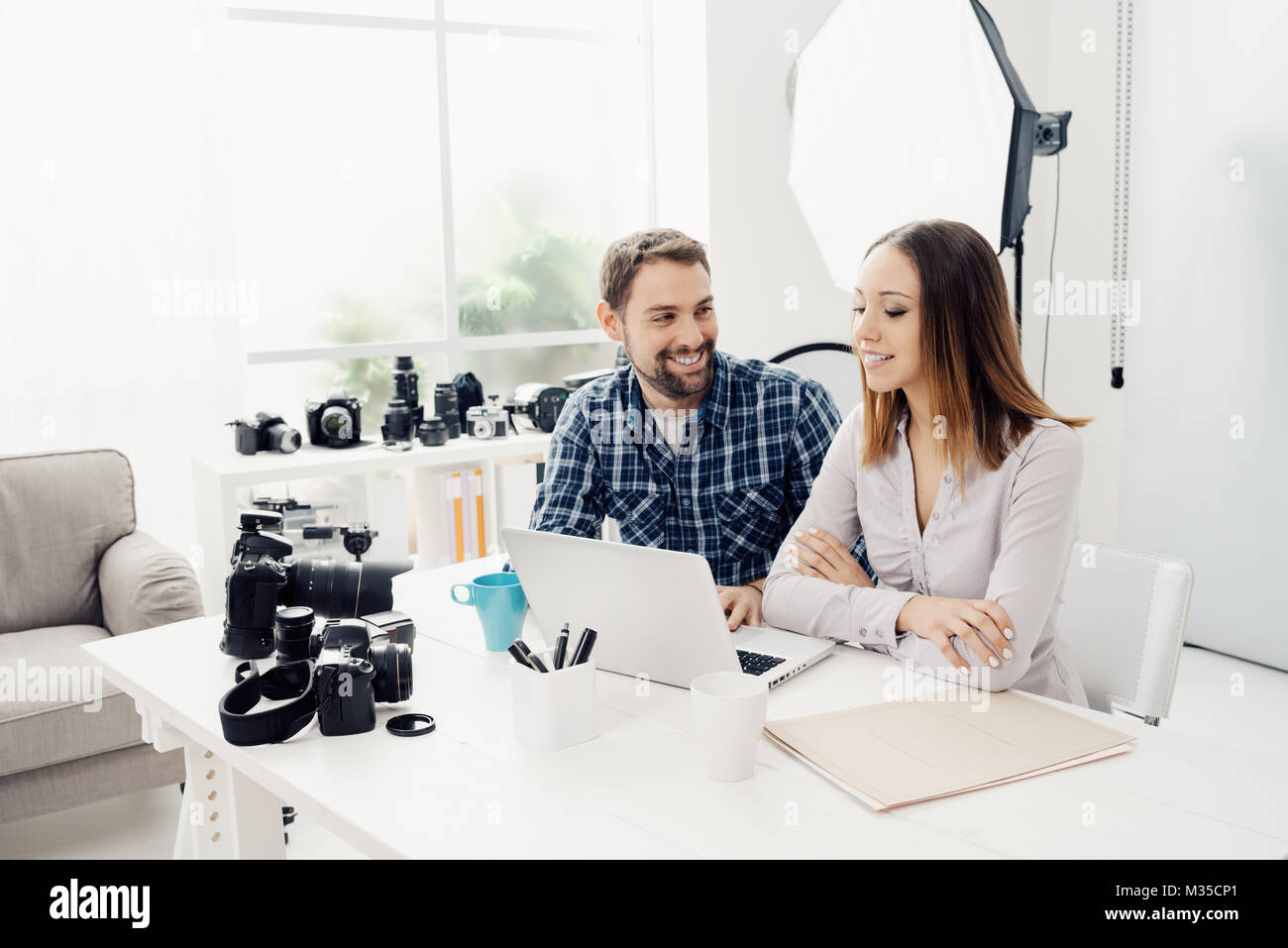 Fotografo e designer in una agenzia creativa, essi sono seduti alla scrivania e lavorare insieme con un laptop Foto Stock