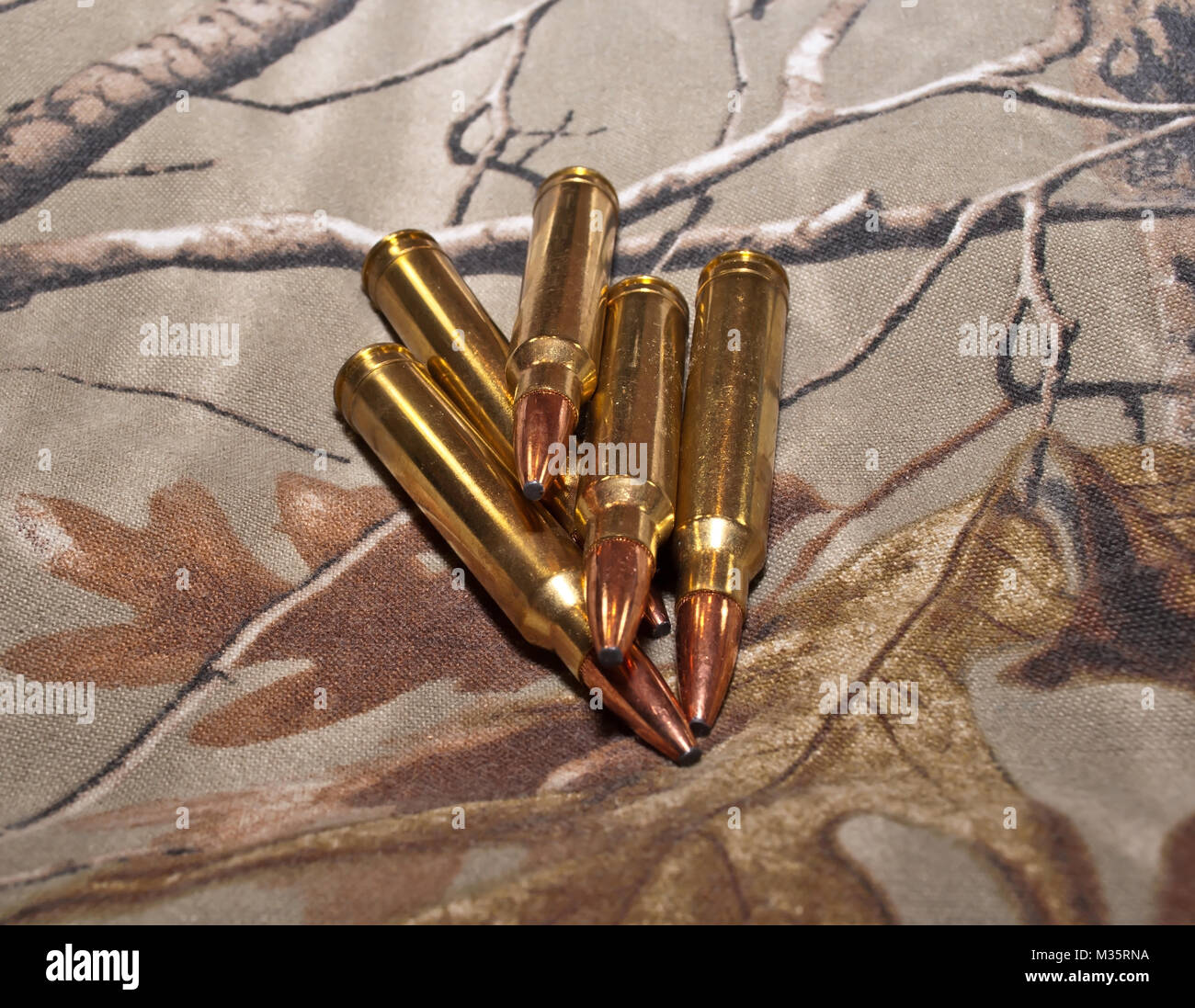 Cinque proiettili di fucile su un sfondo di mimetizzazione Foto Stock