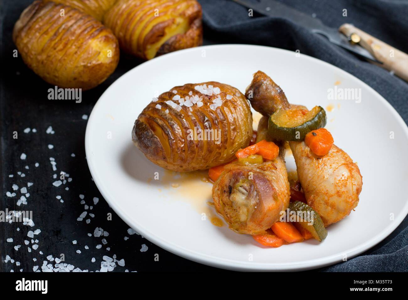 Patate Hasselback come piatto di lato al pollo Cosce di pollo disossate Foto Stock