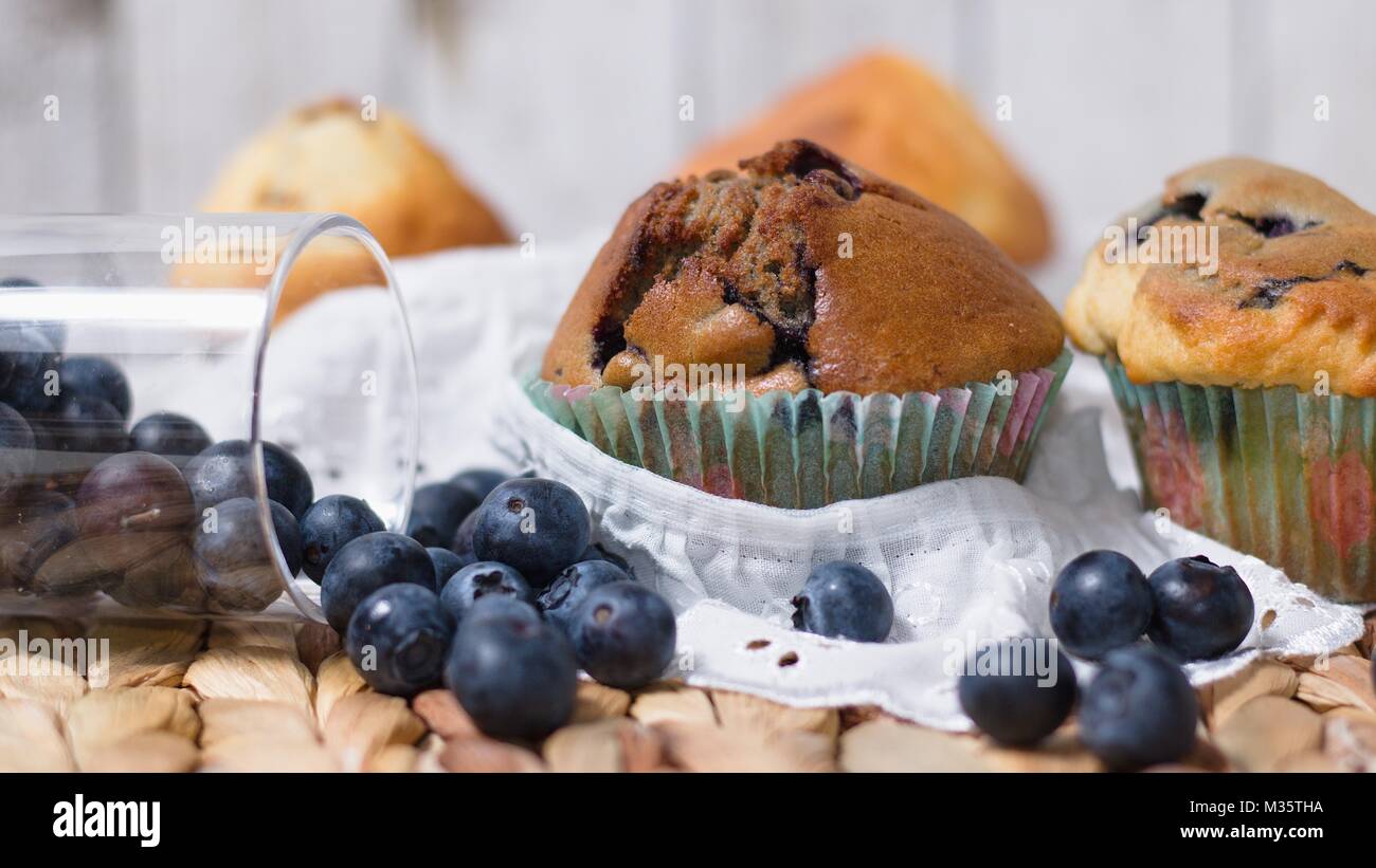 Wide screen shot di rustico snack impostazione. Muffin fatti in casa, mirtilli, pizzo bianco panno. Foto Stock