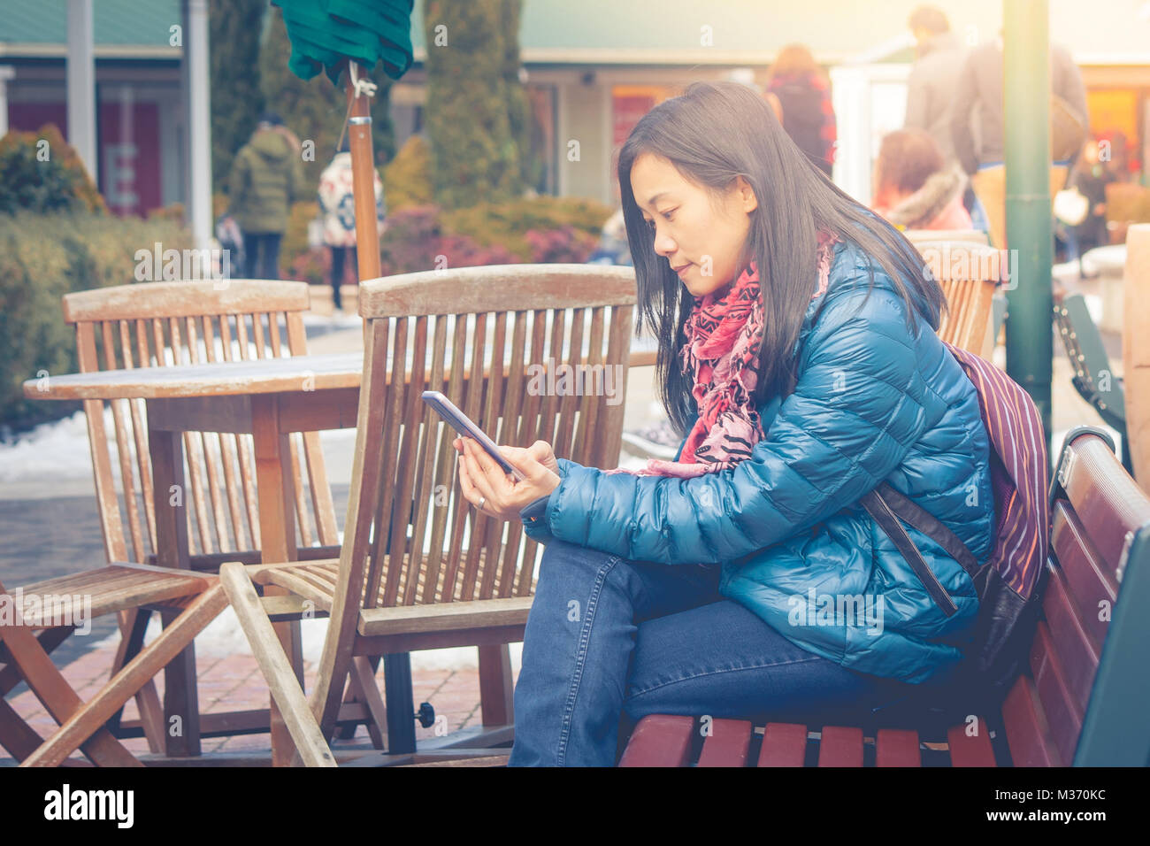 Viaggio vacanza invernale concetto : donna asiatica traveler seduta in legno lungo sedile in corrispondenza al di fuori e giocare il suo smartphone. Foto Stock
