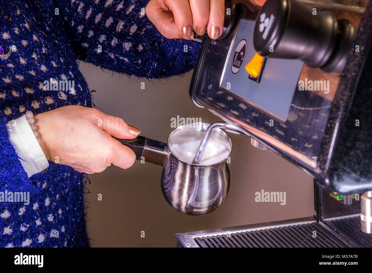 Donna di mano che tiene un acciaio inossidabile per la schiuma di latte caraffa, sotto il vapore / lancia vapore di una commerciale macchina espresso, per creare la schiuma. Regno Unito. Foto Stock