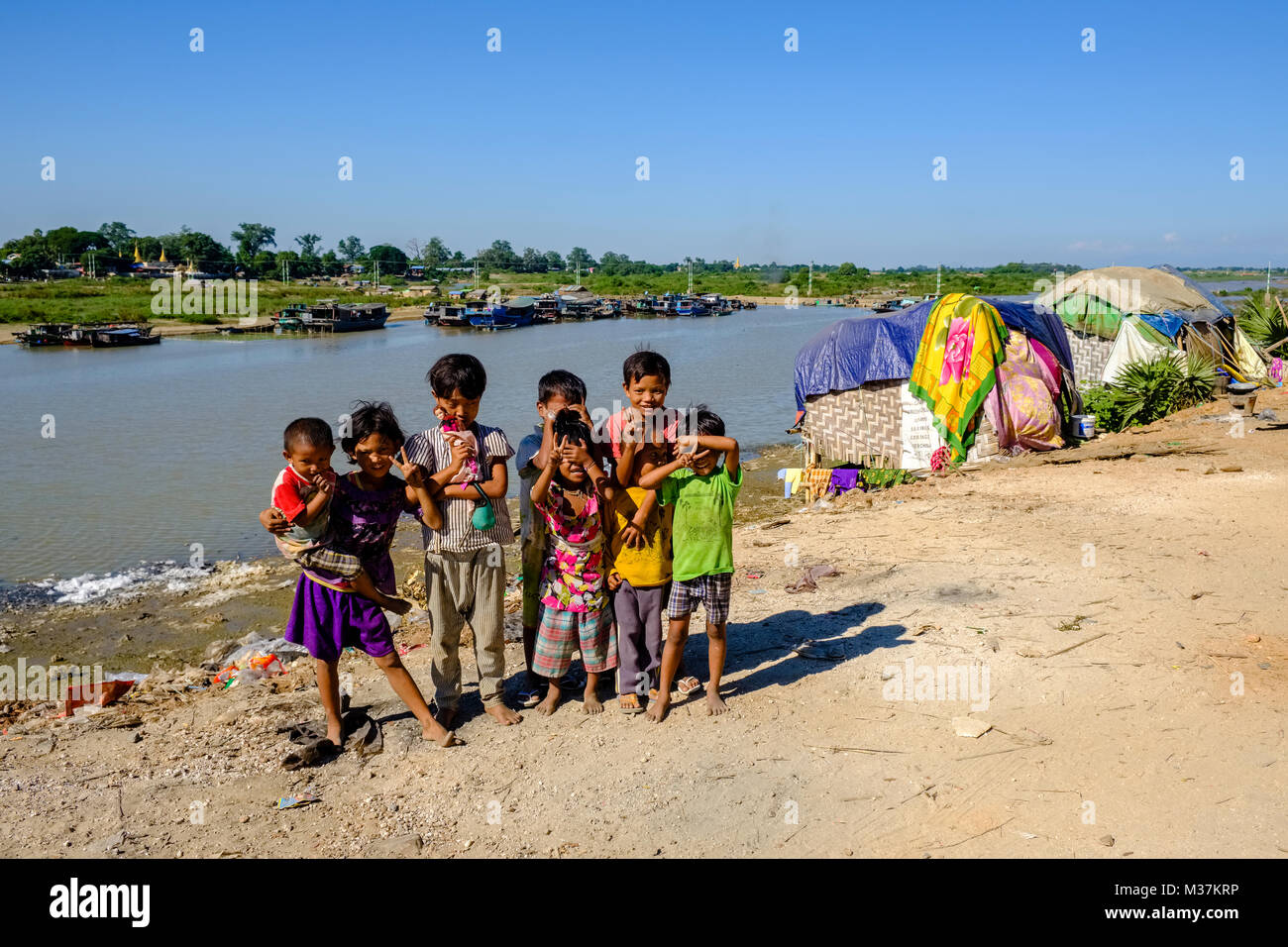 I bambini giocano nella parte anteriore delle baracche baraccopoli alla periferia della città nei pressi del fiume Irrawaddy Foto Stock