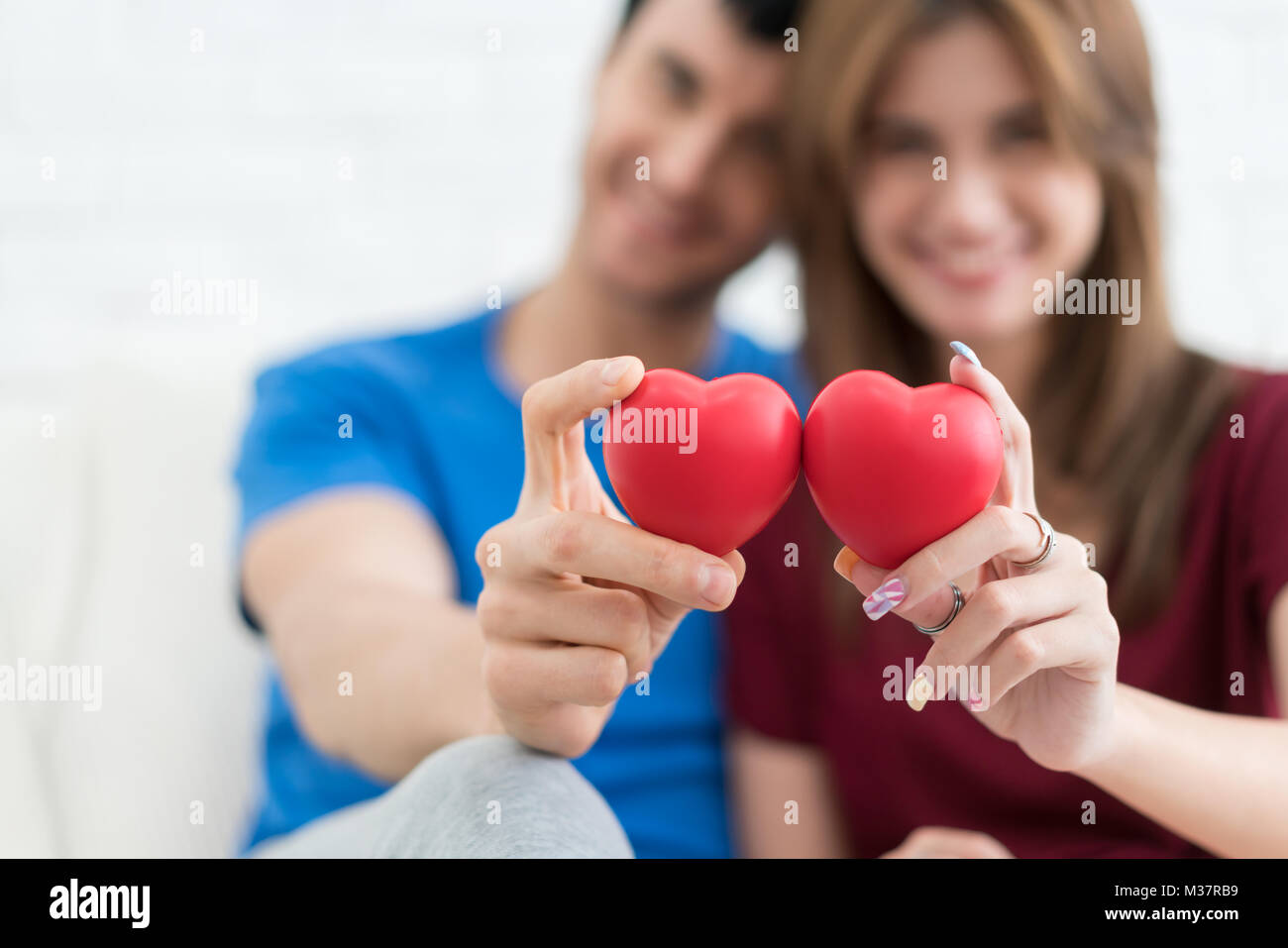 Carino coppia seduta tenendo cuore rosso in poltrona a casa. Coppia felice in amore. Il giorno di San Valentino. Foto Stock