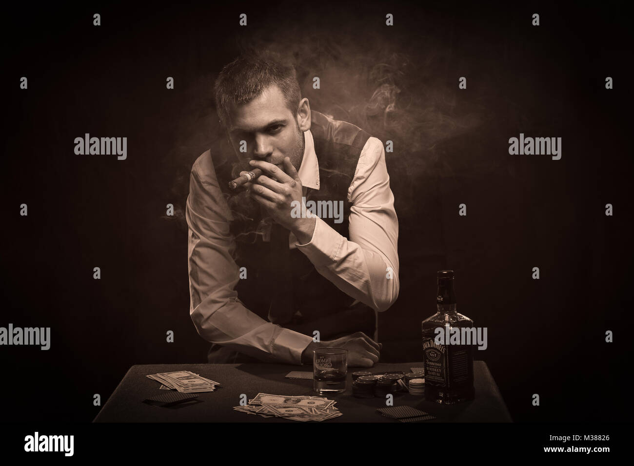 Tormentata gangster che fuma un sigaro e beve whisky al tavolo da poker Foto Stock