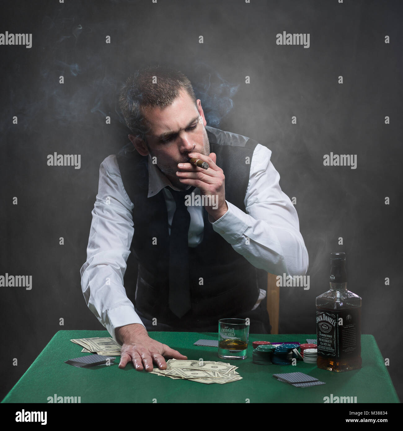 Tormentata gangster che fuma un sigaro e beve whisky al tavolo da poker Foto Stock