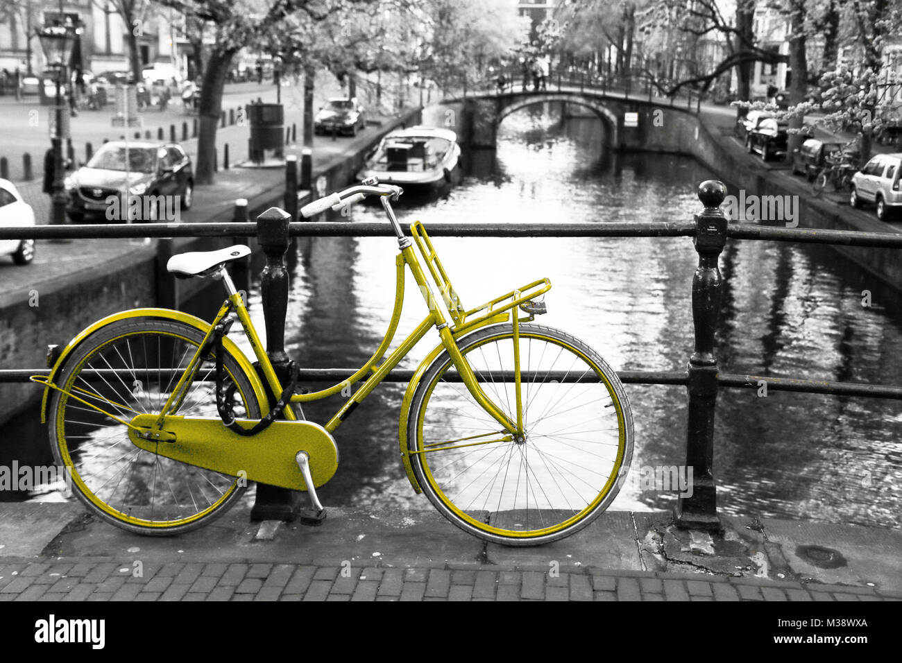 Una foto di una solitaria bici gialla sul ponte sul canale di Amsterdam. Lo sfondo è bianco e nero. Foto Stock