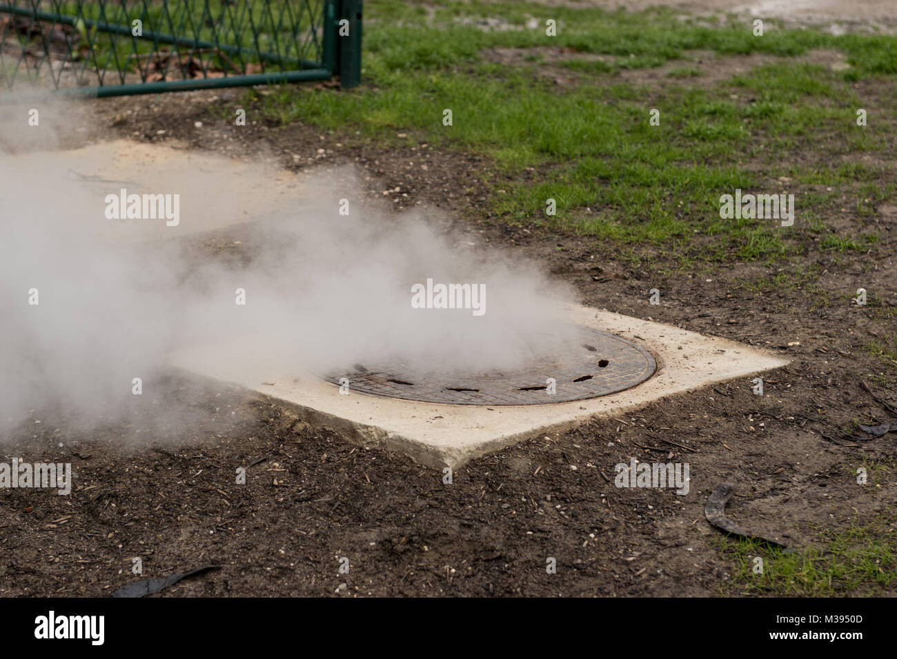Bianco caldo vapore che fuoriesce di metallo del tombino o botola di metallo Foto Stock