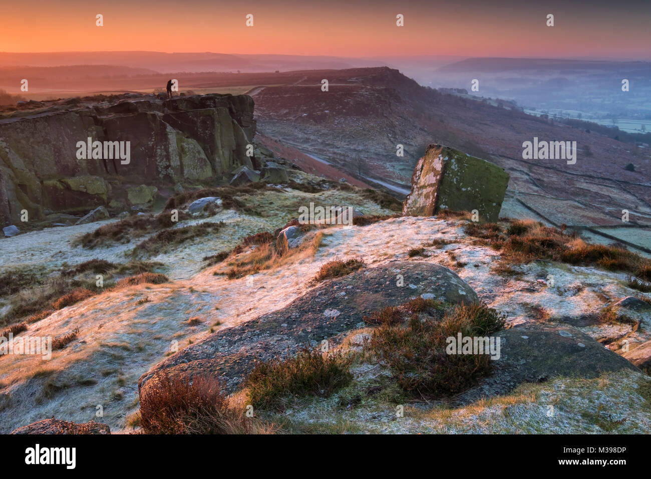 Un fotografo sorge all'alba sul coperto di brina Curbar Edge in inverno, nei pressi di Calver, Parco Nazionale di Peak District, Derbyshire, England, Regno Unito Foto Stock