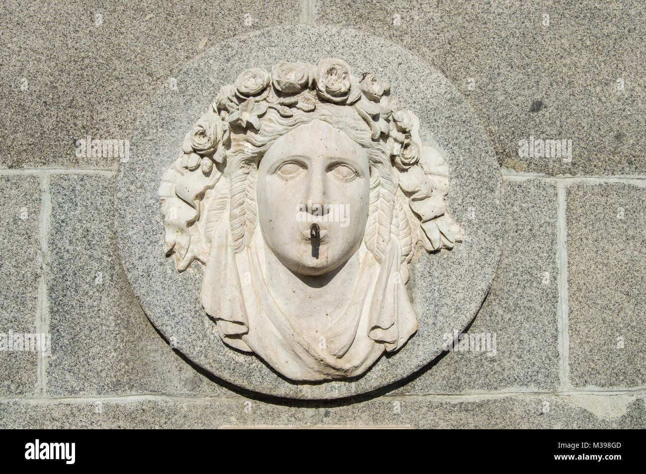 Medaglione di pietra con volto coronato con rose sulla parete di una fontana in Madrid. Spagna Foto Stock