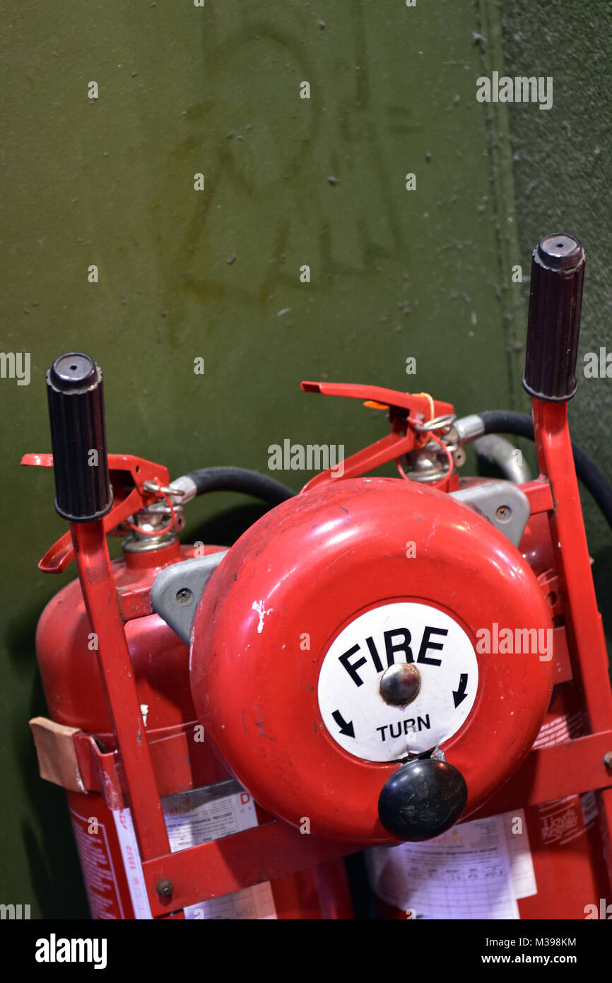 Una mano fire il campanello di allarme su un carrello con gli estintori per domare gli incendi e interventi di emergenza quando il fuoco scoppia. alrms e avvisi. Foto Stock