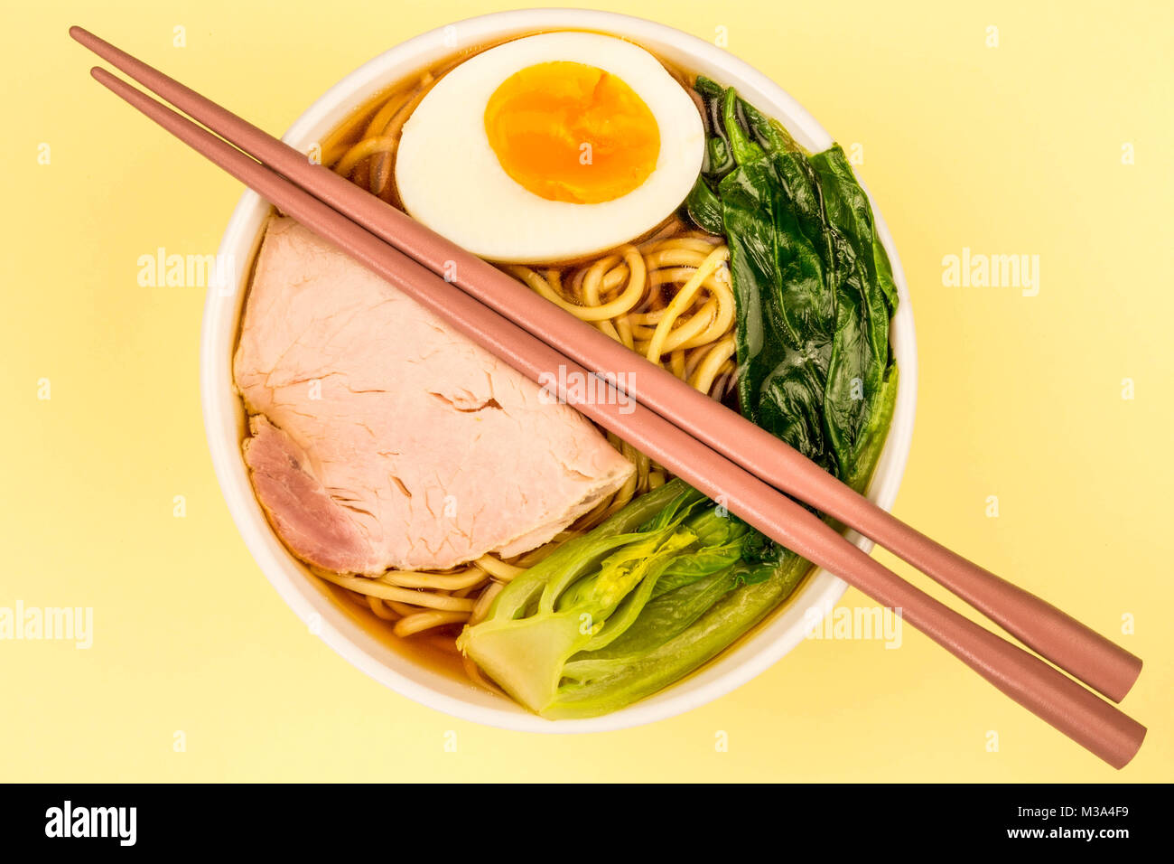 Ciotola di stile Giapponese la carne di maiale Ramen noodle soup con pak choi e un uovo sodo contro un pallido sfondo giallo Foto Stock