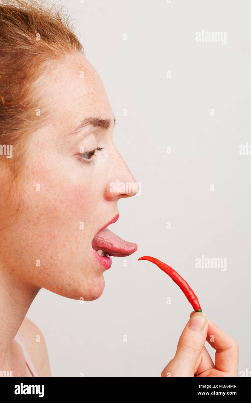 Modello rilasciato. Profilo di donna test del calore di un peperoncino rosso con la sua lingua. Foto Stock