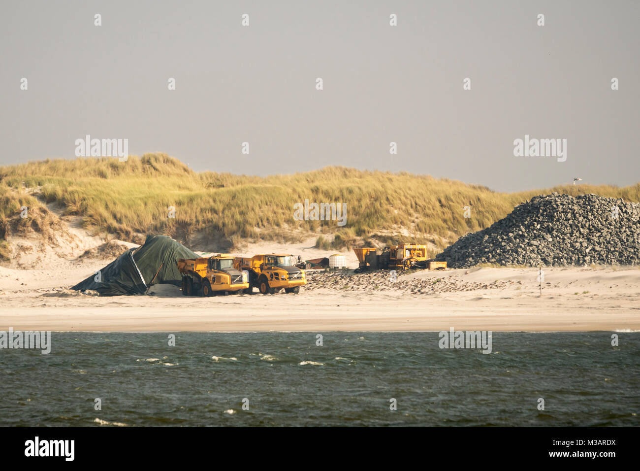 Baumaschinen stehen am Strand bereit für den Küstenschutz der Insel Wangerooge zur Erhöhung und Verstärkung des Dorf- und Ostgrodendeiches Foto Stock